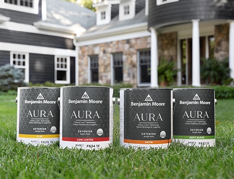 Four cans of AURA® Exterior paint on a front lawn.