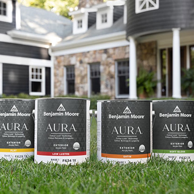 Four cans of AURA® Exterior paint on a front lawn.