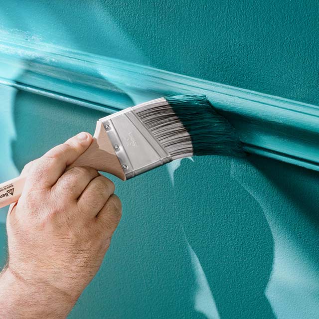A person applies ben Interior paint to a wall using a paintbrush.