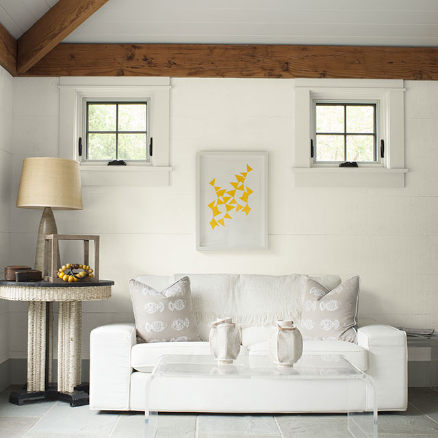 A bright sitting room with white shiplap walls accented by neutral fabric furniture and accessories.