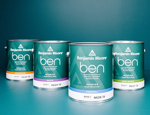 Four cans of ben Interior paint on a blue table in front of a blue painted wall.