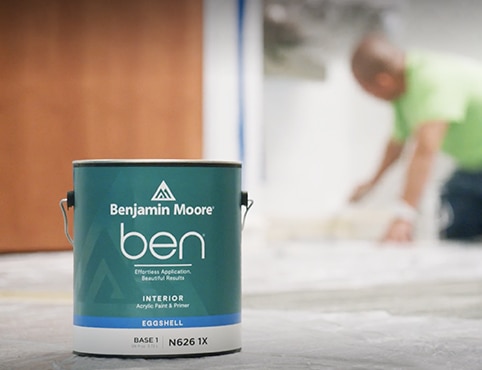 A painting contractor crouches down to paint a wall with ben Interior paint.