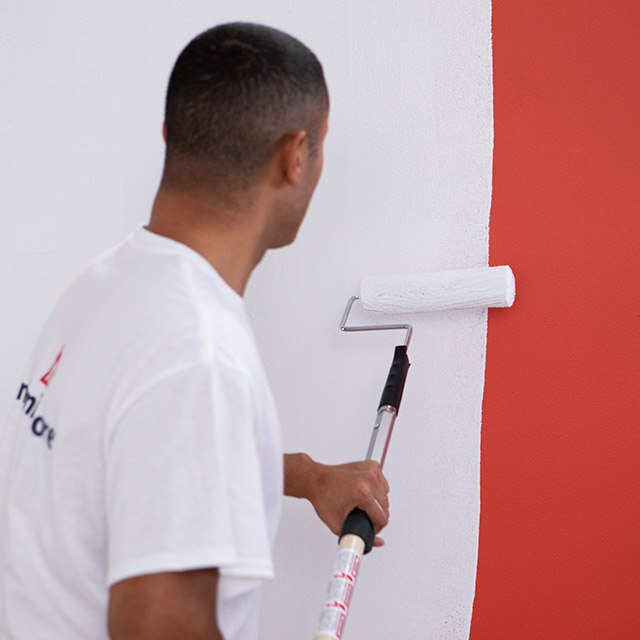 Un entrepreneur en peinture applique un apprêt Avant-Première au rouleau sur un mur peint en rouge.