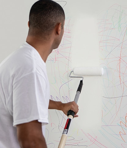A painting contractor rolling Fresh Start® primer over crayon scribbles on a white wall.