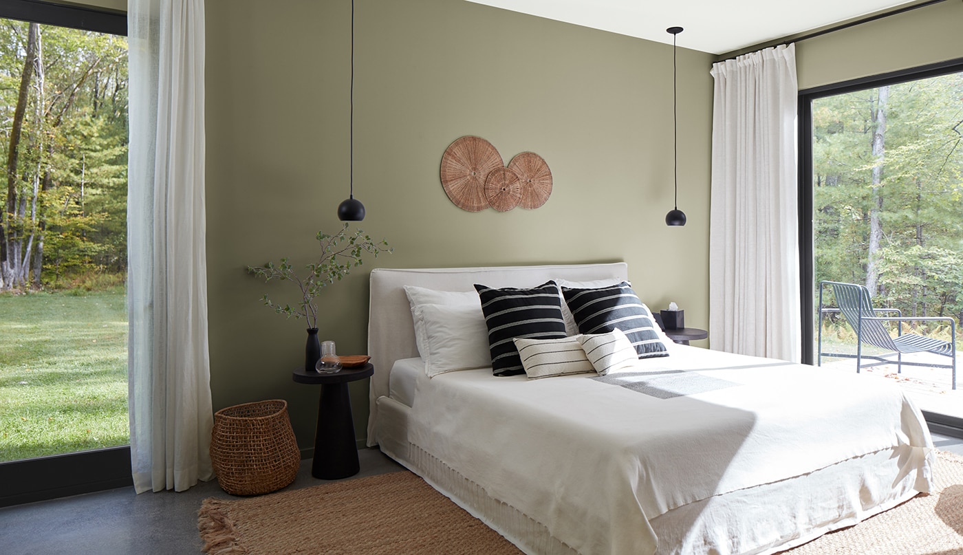 A sunlit bedroom with sage green painted walls, a white ceiling, black-trimmed glass doors, and black and white bedding and decor.