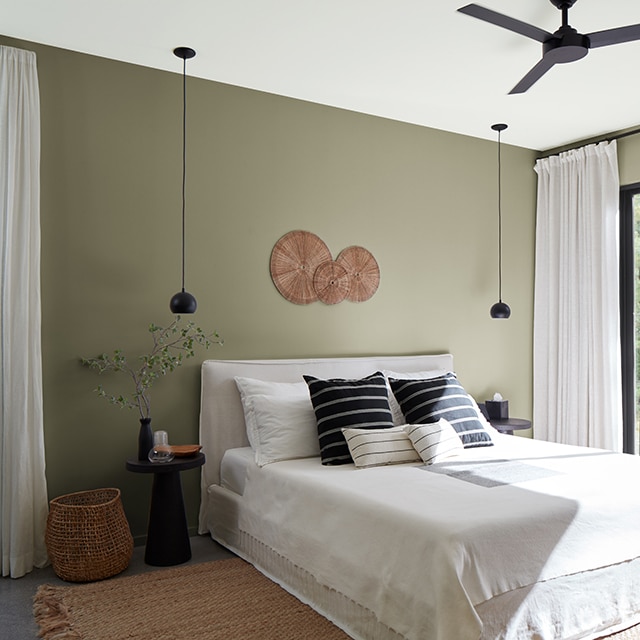 A sunlit bedroom with sage green painted walls, a white ceiling, black-trimmed glass doors, and black and white bedding and decor.