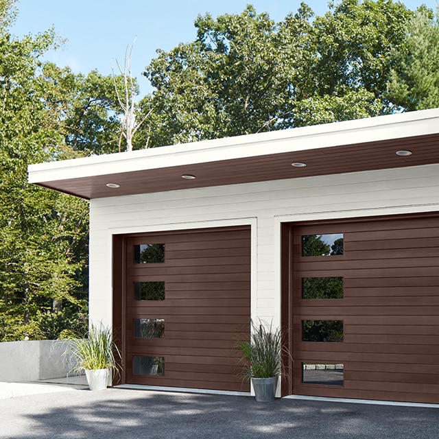 A closed two-car garage with white siding, dark brown garage doors, and potted plants.