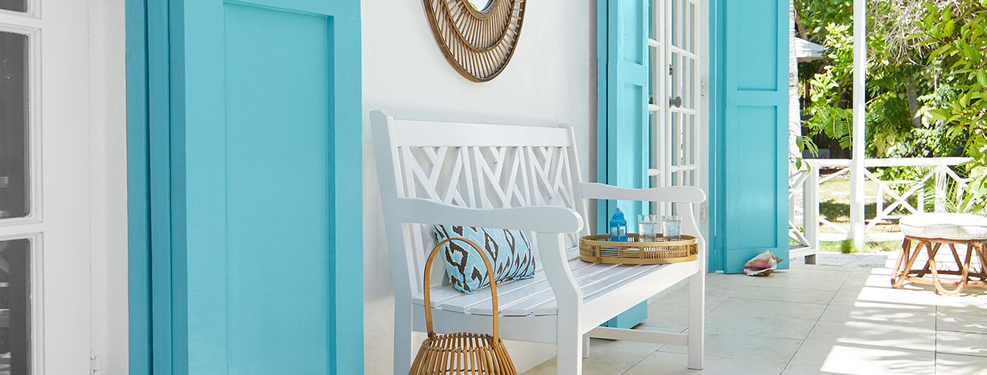 A porch against a white exterior with wooden doors painted light blue and a white bench.