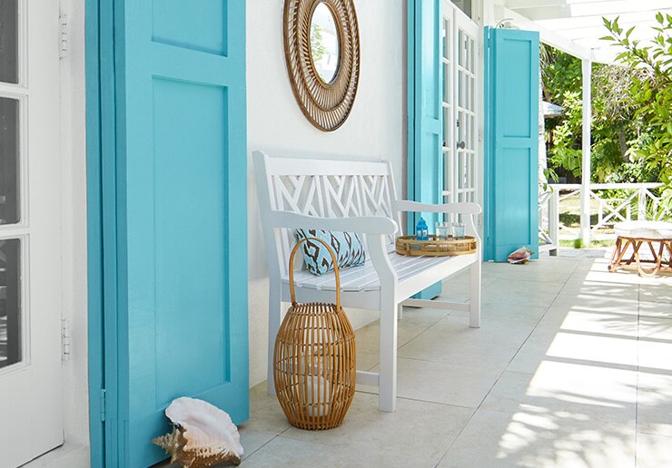 A porch against a white exterior with wooden doors painted light blue and a white bench.