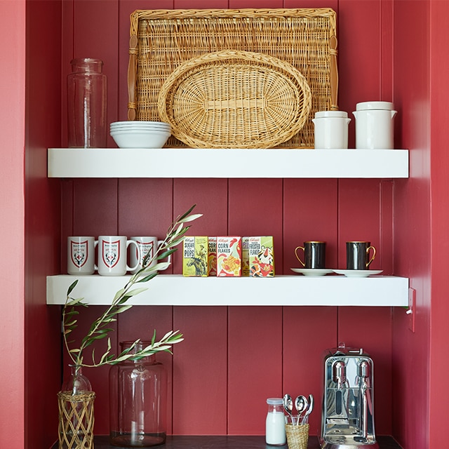 A close-up of white-painted built-in kitchen cabinetry with brass handles, a black countertop, and white-painted shelving holding breakfast cereals and other knick-knacks.
