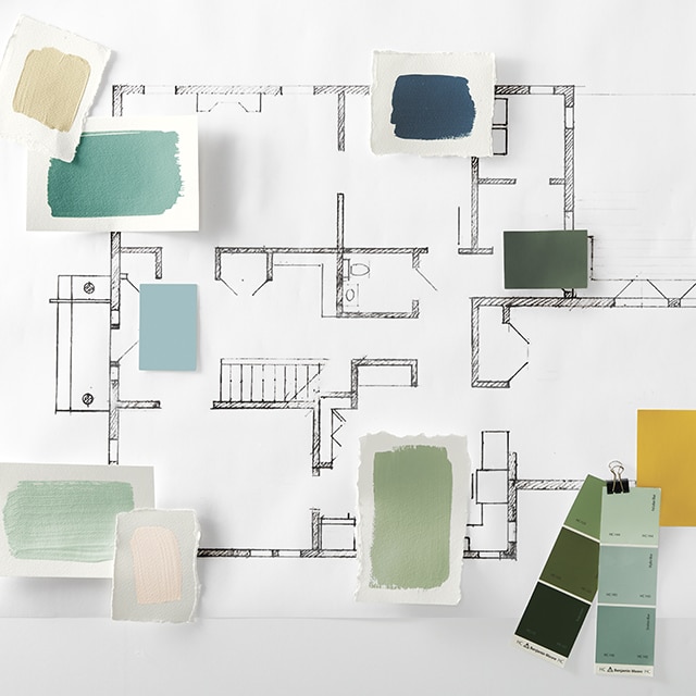 A floor plan with shades of green and blue paint samples placed on top, along with multiple open cans of green paint and a paint brush.