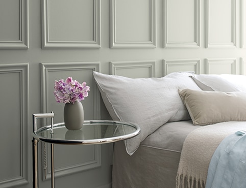 A gray bedroom wall with a glass bedside table.