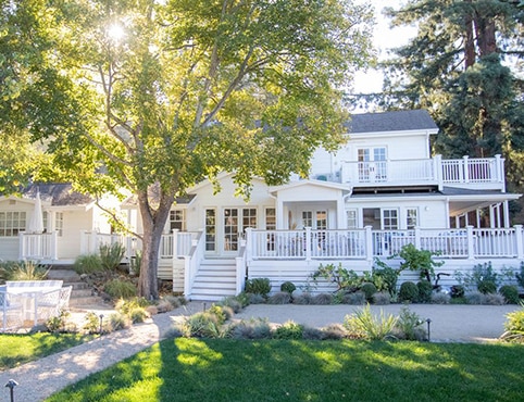 Beautiful, white-painted landmark Hoopes farmhouse with french doors, wraparound porches and stairs, surrounded by lush greenery.