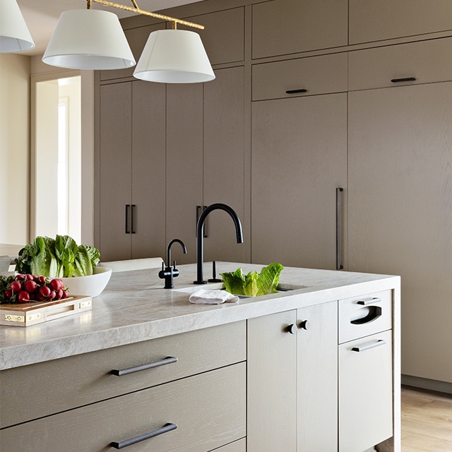 A kitchen with beige cabinets, a marble-topped island, and a painted off-white ceiling is dramatically illuminated by a single source of lighting.