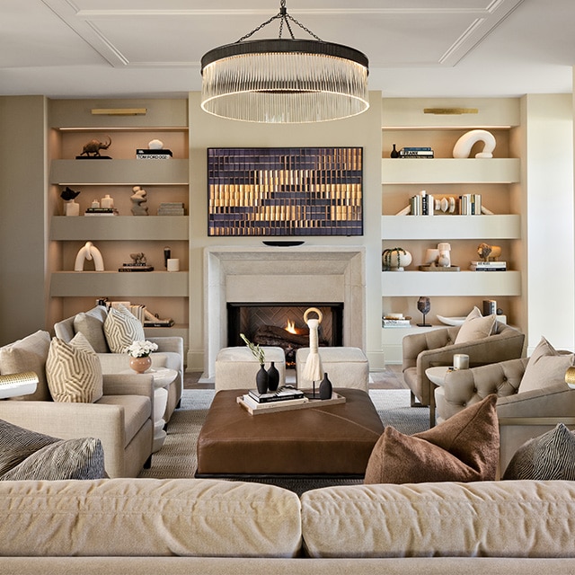 A large living room with painted off-white walls, a white paint ceiling, and recessed shelving, with furniture and decorations framing a fireplace.