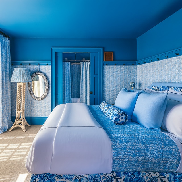 Una habitación pintada en azul, con papel pintado azul con diseño, y ropa de cama y decoración en azul y blanco.