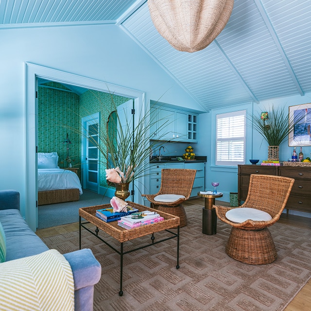 Una sala de estar pintada en azul cielo, con techo abovedado con revestimiento y decoración costera, conectada a una habitación trasera con papel pintado verde.