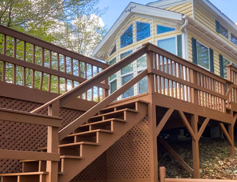 Stairs leading up to the deck of a beige house with large windows.