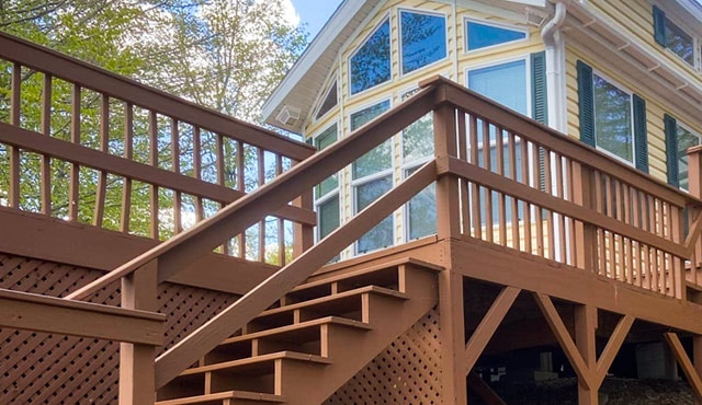 Stairs leading up to the deck of a beige house with large windows.