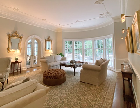 The after photo of a living room remodel featuring light gray walls with an arched doorway and wall to wall curved windows.