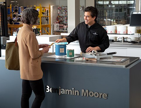 A Benjamin Moore store owner helps a home owner purchase paint.