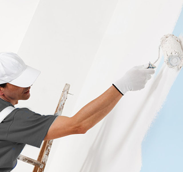 A professional painter uses a paint roller to apply white paint on a wall.