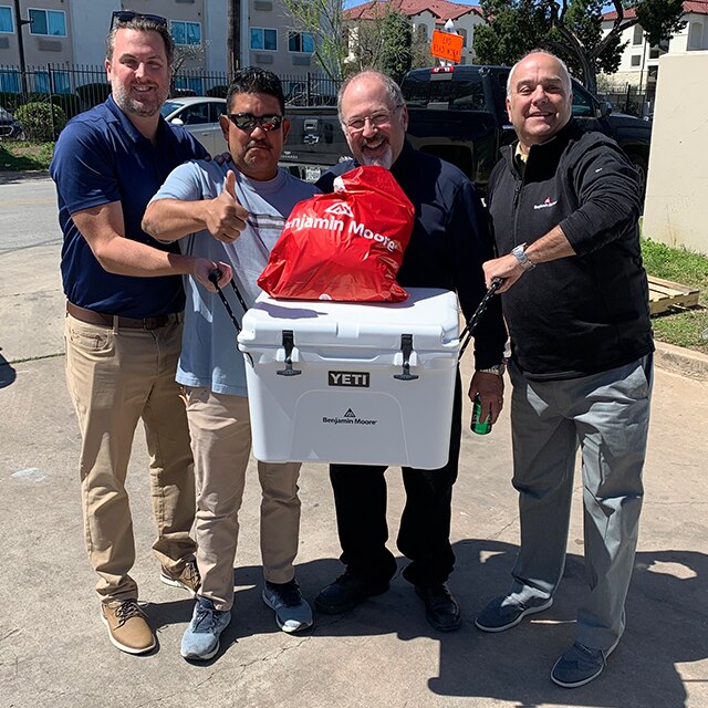 Four men holding a Yeti cooler and Benjamin Moore goodie bag smile for the camera.
