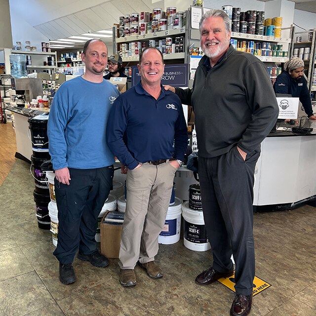 Three men in a locally owned Benjamin Moore retail location during Contractor Appreciation week stand in front of paint cans.
