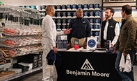 Four men gathered around a display table with Benjamin Moore product guides, brochures, and color fan decks, in a locally owned Benjamin Moore store.