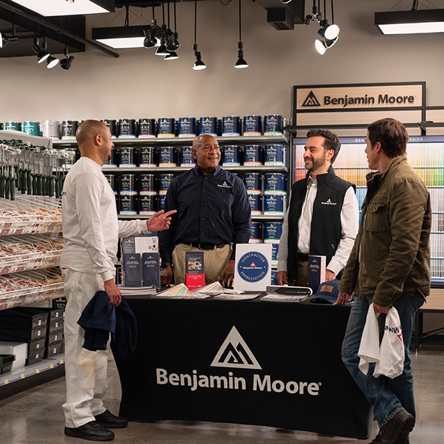 Four men gathered around a display table with Benjamin Moore product guides, brochures, and color fan decks, in a locally owned Benjamin Moore store.