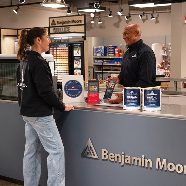 Un homme et une femme se trouvent au comptoir d’un magasin Benjamin Moore où sont posés des contenants de Regal🅫 Select et des brochures Contractor Rewards.