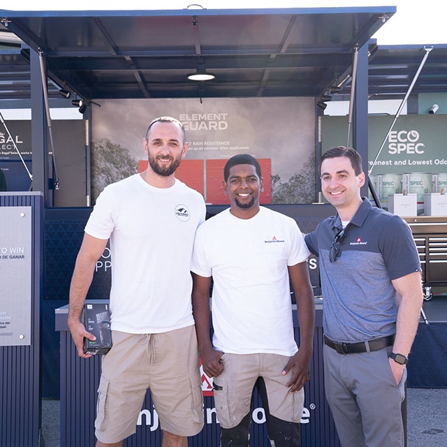 Three men posing in front of Benjamin Moore outdoor displays with Regal Select®, Element Guard®, and Eco Spec® backdrops.