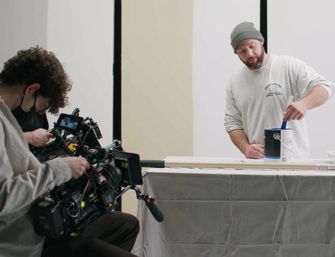 A gallon of AURA® Interior paint in eggshell on a tarp with a painting contractor standing in the background.