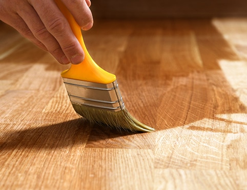 Un peintre professionnel applique la finition à un parquet de bois franc.