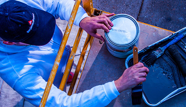 Un peintre détenant une licence et portant une casquette Benjamin Moore se tient près d’un échafaudage.