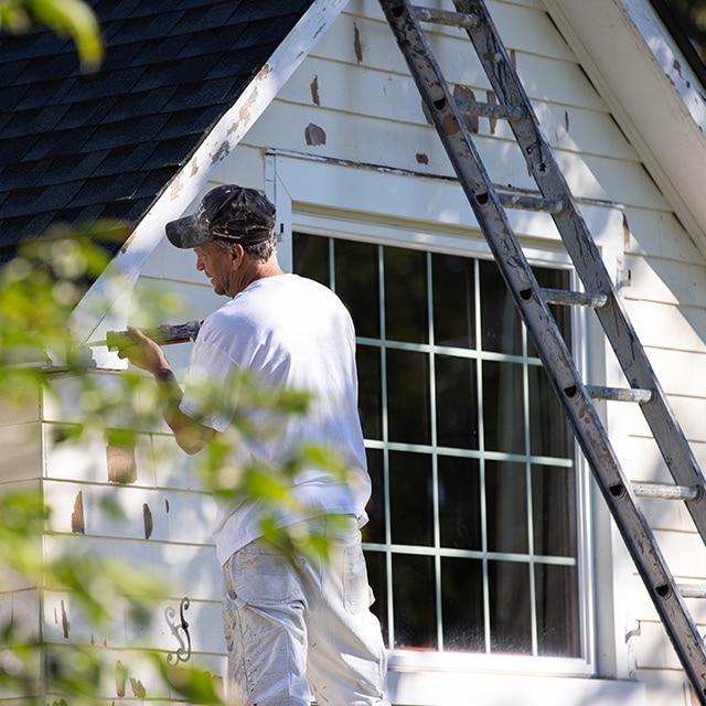 Man in a white shirt repairing the siding of a house.