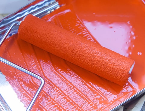 A roller cover resting in a roller tray coated with red paint