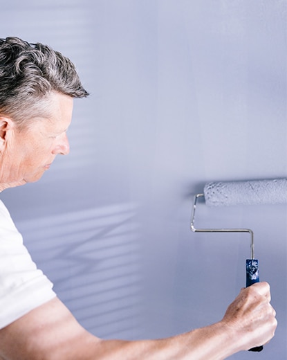 A painting contractor applies light blue ben Interior paint to a wall using a paint roller.