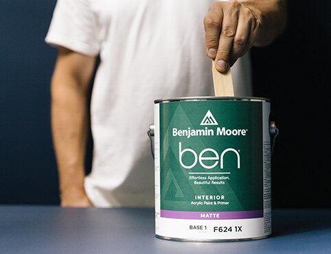 A painter stirs a can of ben Interior paint.
