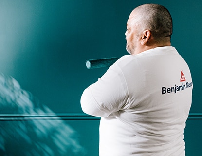 A painting professional observes a teal-coloured wall he painted using ben Interior paint.