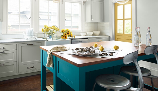 Bright, sun-drenched kitchen with painted yellow door and teal island