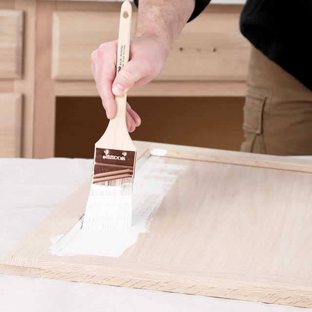 A contractor applying a bonding primer to a cabinet door with a brush