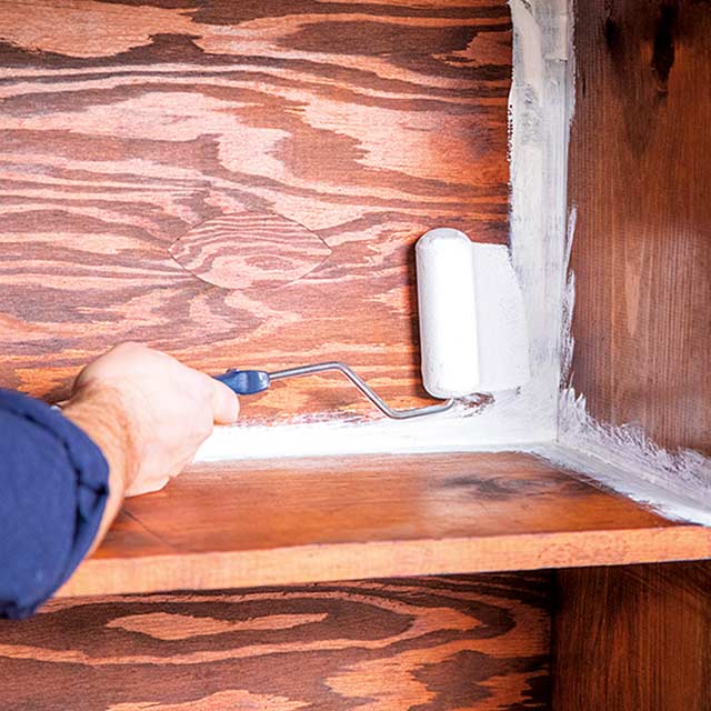L'intérieur d' une étagère en bois est recouverte au rouleau par un entrepreneur peintre professionnel