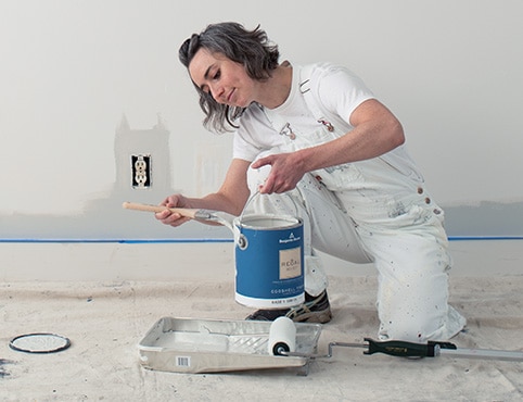 Une femme tenant un contenant de peinture d’intérieur REGALMD Select de couleur blanche.