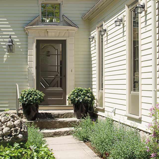 L'extérieur d'une magnifique demeure avec une porte d'entrée brun foncé, un parement blanc cassé et un aménagement paysager soigné.