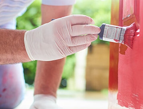 A painting contractor applies red paint to a surface.