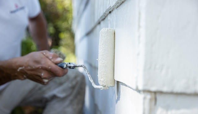 A professional painter rolls Benjamin Moore INSL-X Peel Bonding Primer onto a home exterior.
