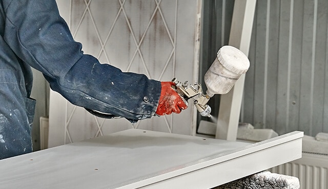 Un entrepreneur en peinture pulvérise une porte d’armoire avec un pulvérisateur à haut volume et à basse pression.