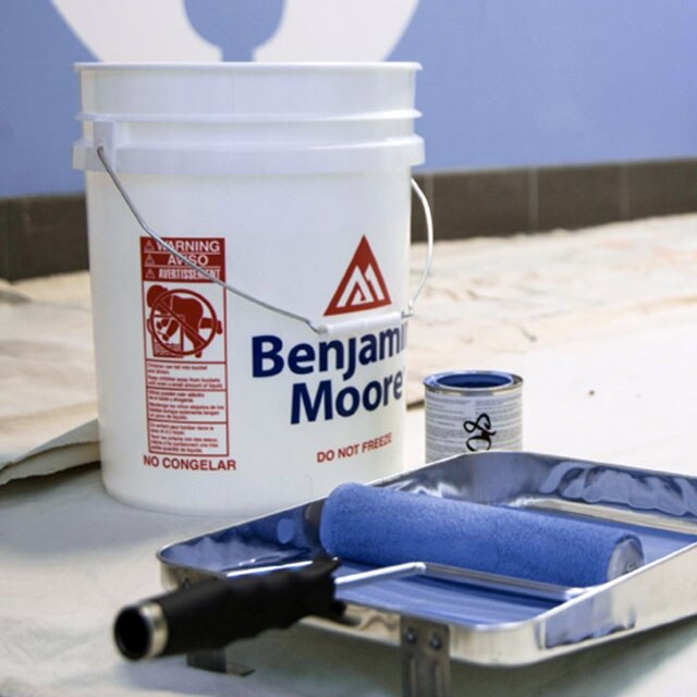 Benjamin Moore® 18.9-L paint bucket sitting next to a roller cover and tray