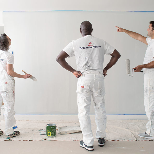 Three painting contractors look at a painted wall